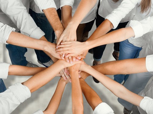 Das Bild zeigt mehrere Personen, die im Kreis stehen und die Hände zur Mitte ausstrecken.