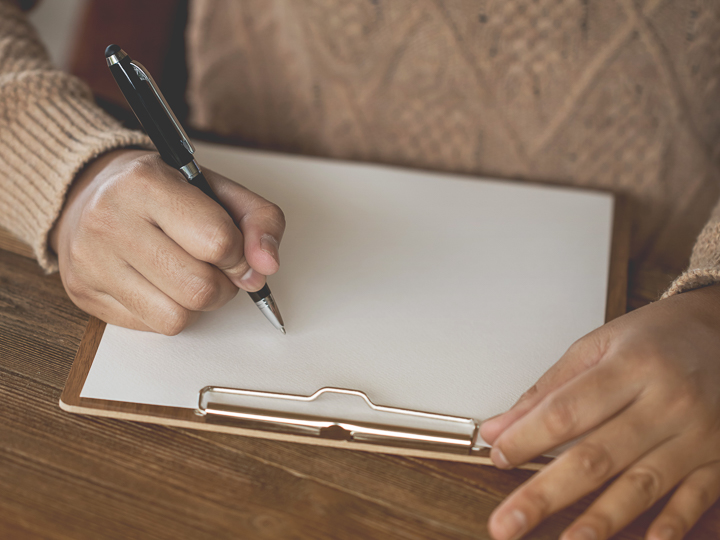 Das Bild zeigt eine Person, die mit einem Stift auf einem Blatt Papier schreibt.